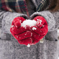 Girl wearing red covered gloves holding snow with Merry Christmas greeting